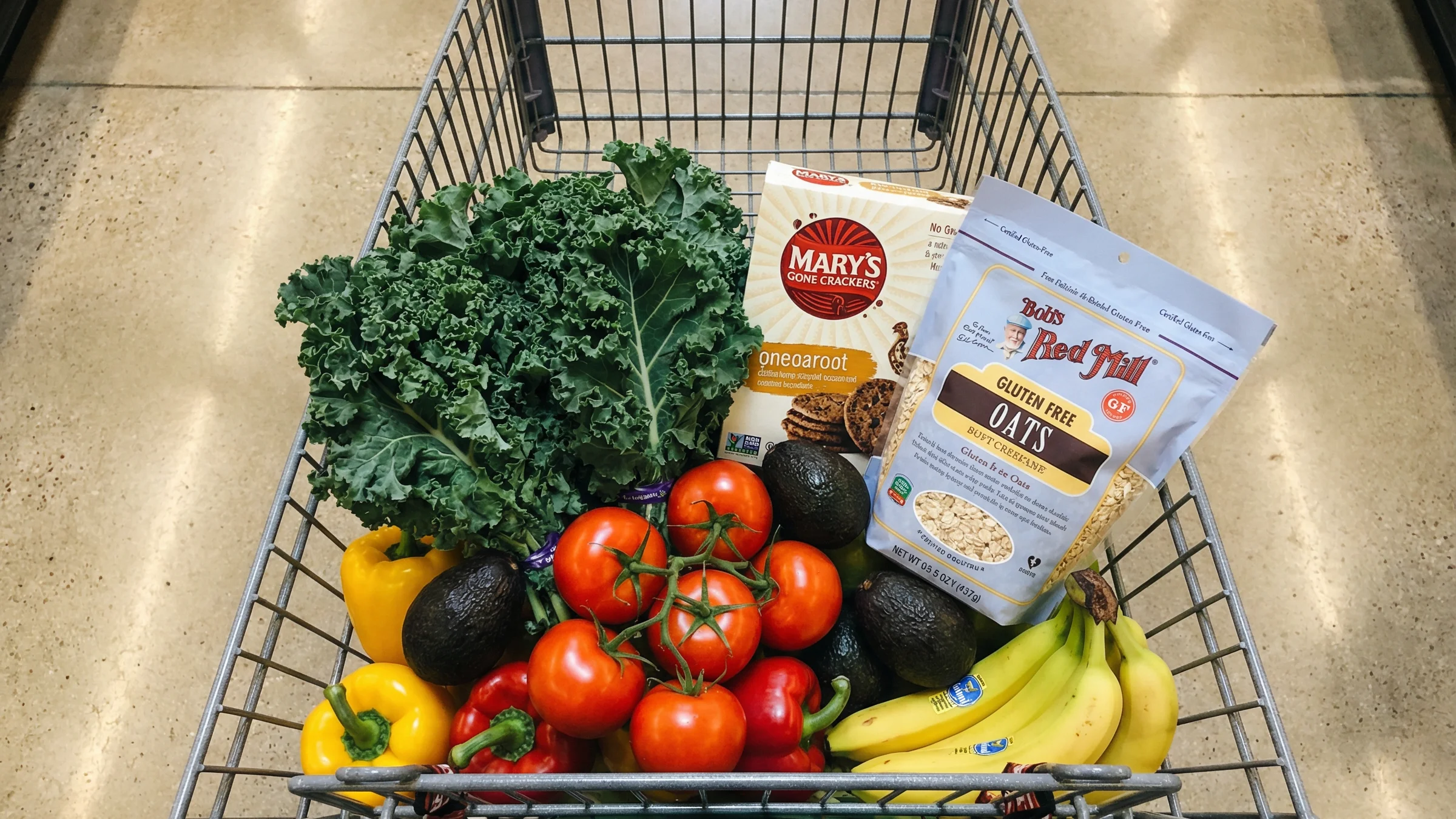 A grocery cart filled with fresh produce and certified gluten-free packaged products including Bob's Red Mill Gluten Free Oats.