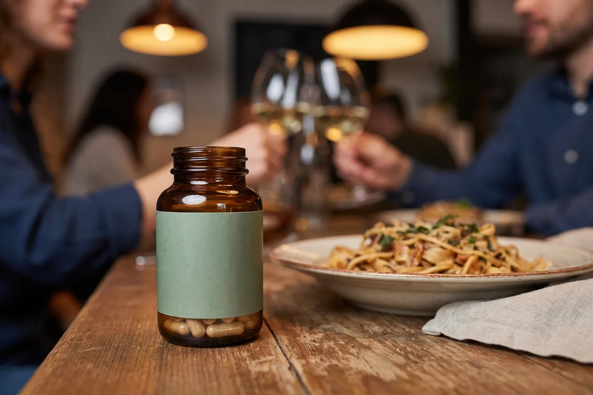 Digestive enzymes for gluten in a supplement bottle beside a meal at a restaurant table
