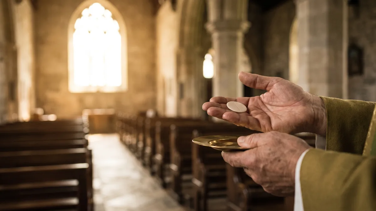 Hands receiving a gluten-free communion wafer over a paten in warm church light