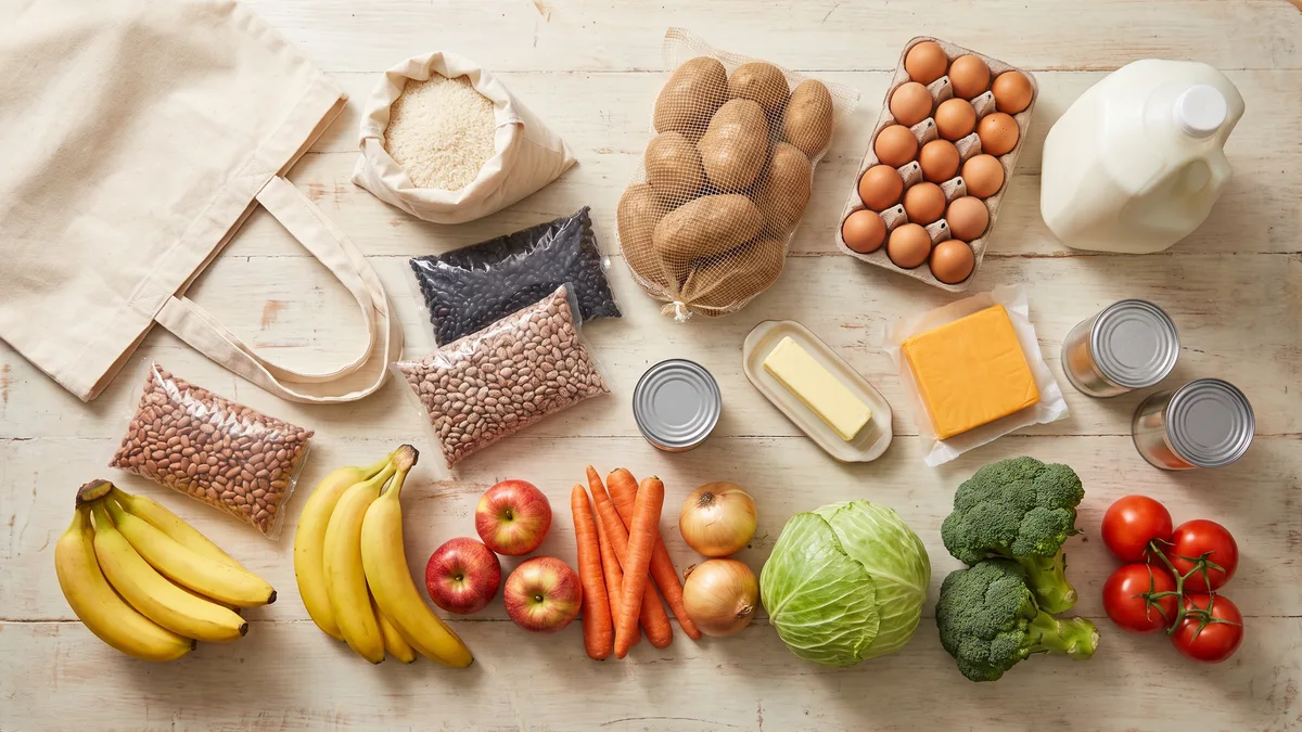 A $100 gluten-free grocery challenge cart of rice, dried beans, potatoes, eggs, milk and fresh produce on a kitchen table